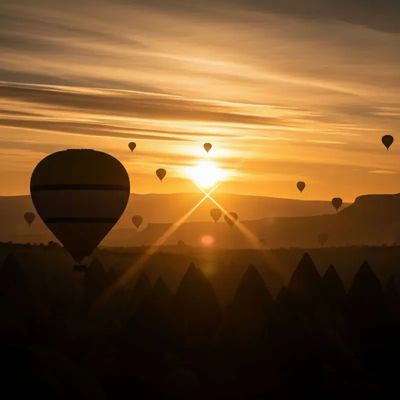 Silhouettes of numerous hot air balloons rising over Cappadocia’s fairy chimneys at sunrise